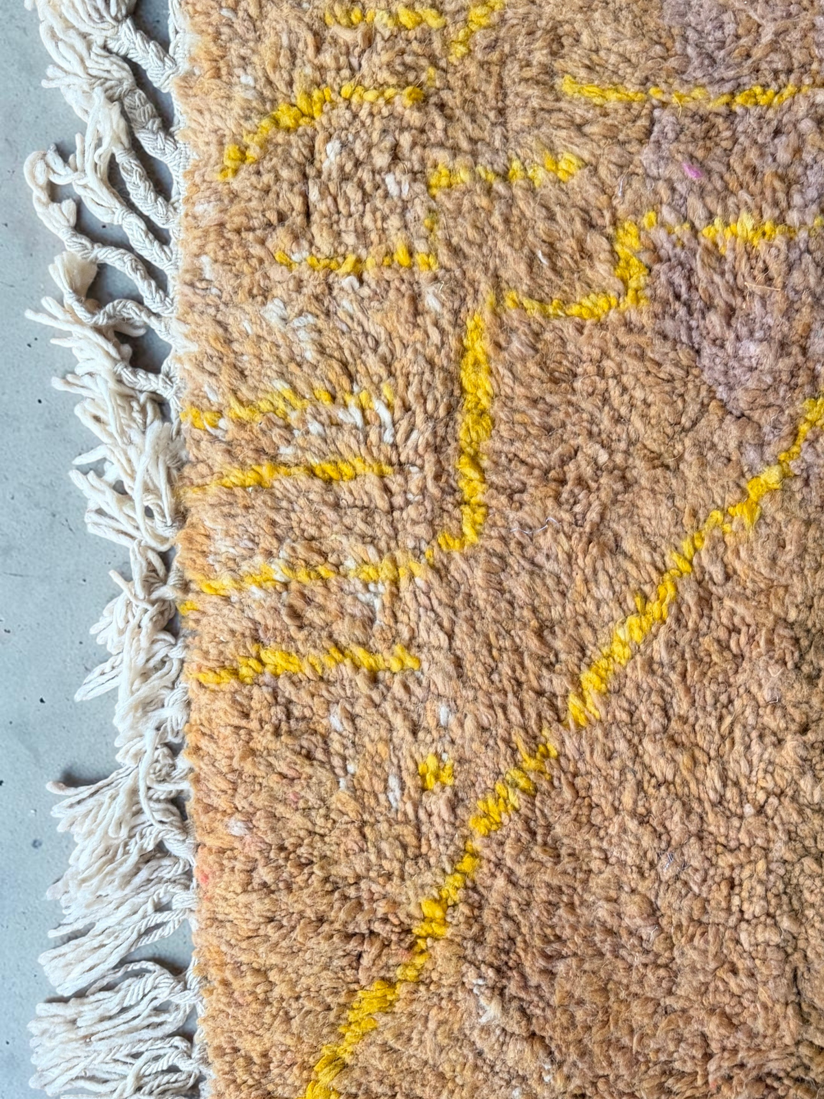 Gros plan sur un tapis YAAS Beni Ouarain en laine naturelle, motifs géométriques jaune solaire sur fond ocre et brun.