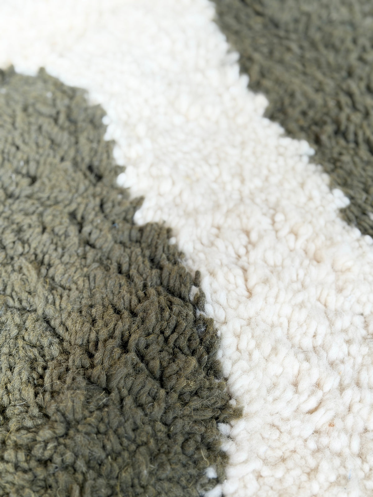 Gros plan sur la texture en laine douce du tapis berbère YAAS avec des motifs géométriques vert olive et crème