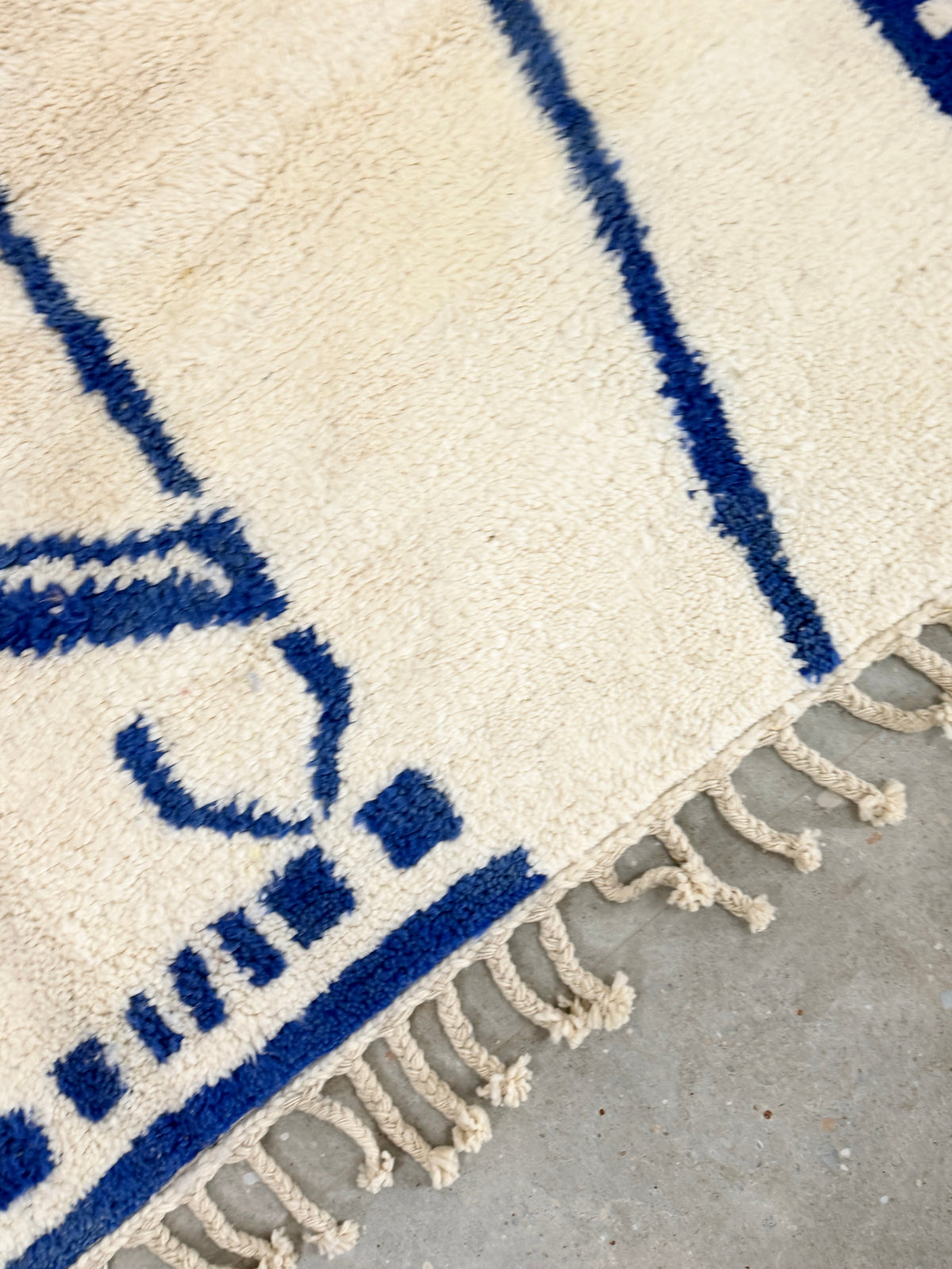 Tapis YAAS en laine de mouton crème avec motifs géométriques bleus et franges, collaboration avec UHORAKEYE