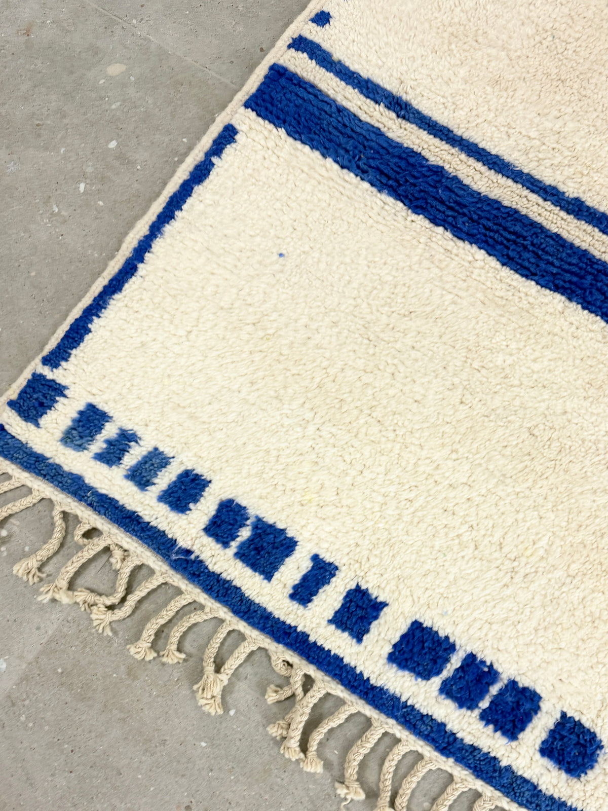 Tapis YAAS en laine de mouton crème avec motifs géométriques et rayures bleu vif, finition à franges artisanale